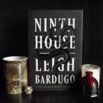 A hardcover copy of Ninth House sits next to a mug that shows the long room at trinity college.